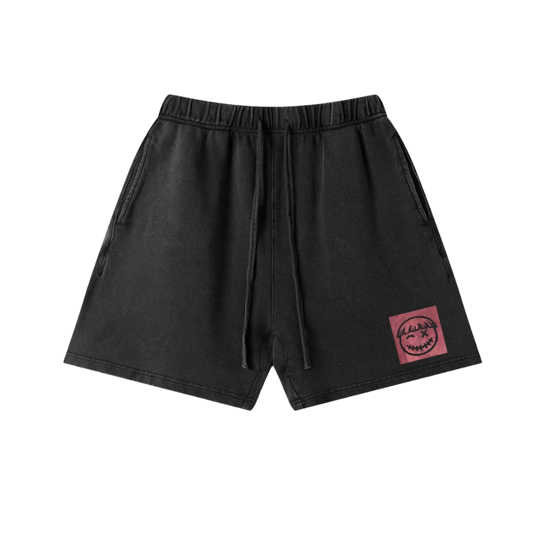 Black cotton graphic shorts — front, PM smiley framed in a small pink square on the hip